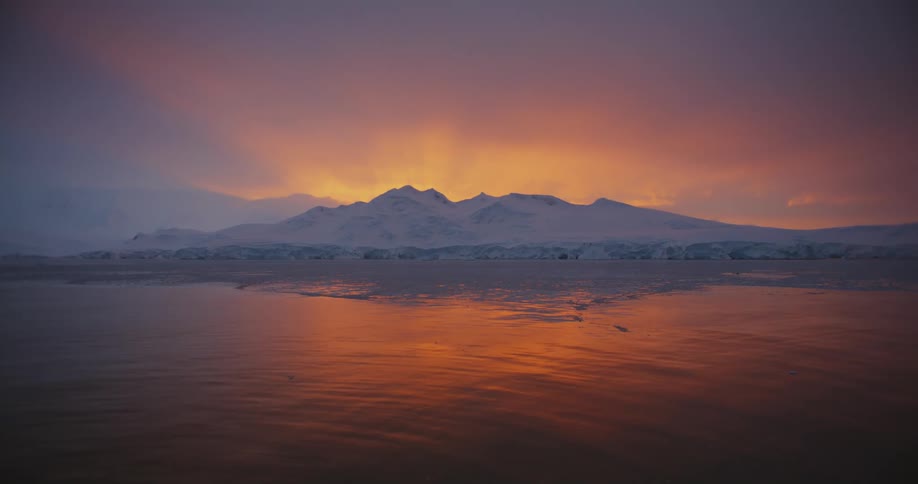 The sun is rising on the mountains by the shore