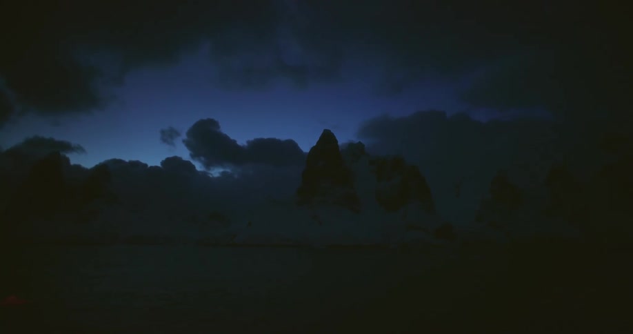 Silhouette of a mountain and the reflection of dark clouds can barely be seen on the water in the darkness