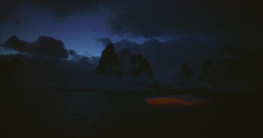 Iceberg floating on the ocean close to the coast at night