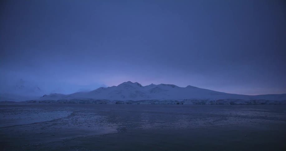 Arctic mountains covered in snow and ice close to the ocean at sunset