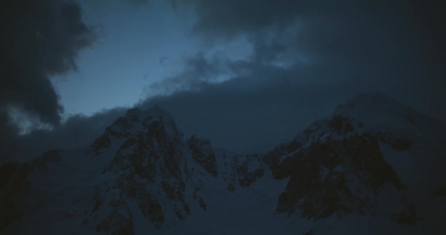 Clouds pass over a snowy mountain ridge at night