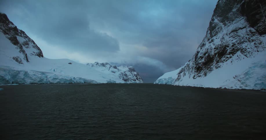 Rippling water leads to snow and ice covered mountains on shore under an overcast sky