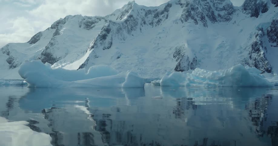 Large chunks of ice floating in clear smooth water near snow covered mountain ridge
