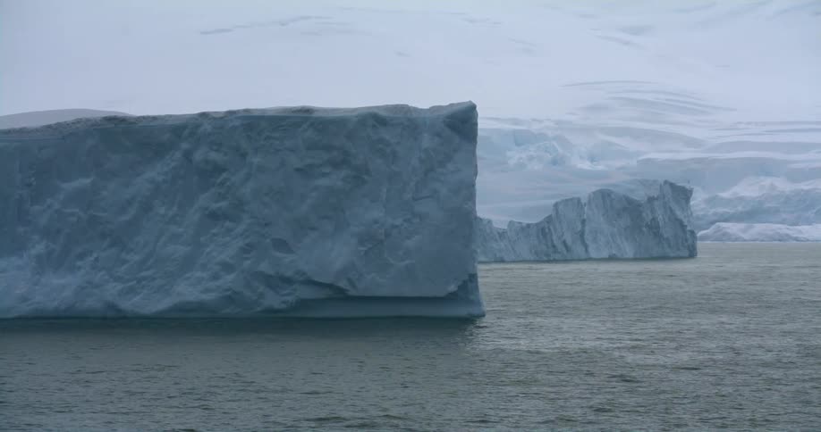 A large piece of ice is floating in the water in front of a snow covered mountain