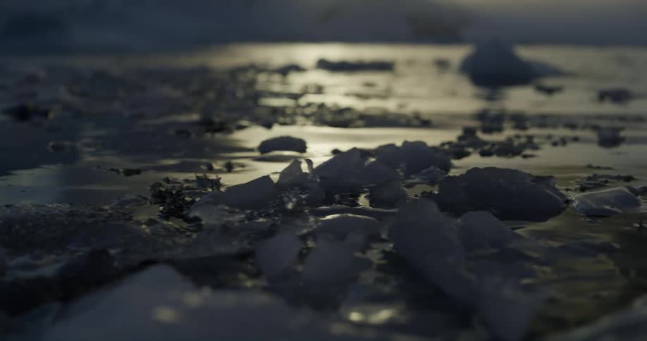Pieces of ice are moving in the water as sunlight reflects on the ripples and waves