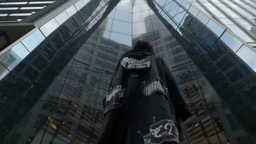 A man stands in front of a mirrored skyscraper and looks up