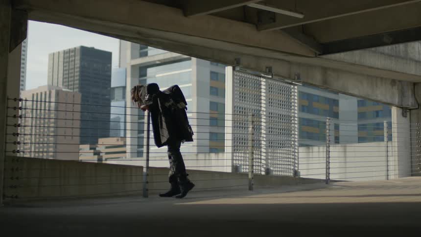 A man leans over a railing and looks below and at the office buildings
