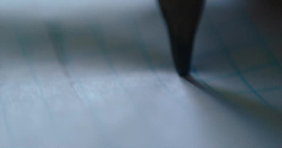 A pen is making a line near blue lines on paper
