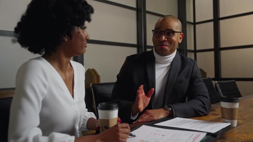 A man and woman sit in a meeting room while enthusiastically reviewing some documents