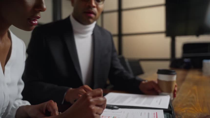 Two people sit at a table in a office meeting room while discussing a document thats being signed