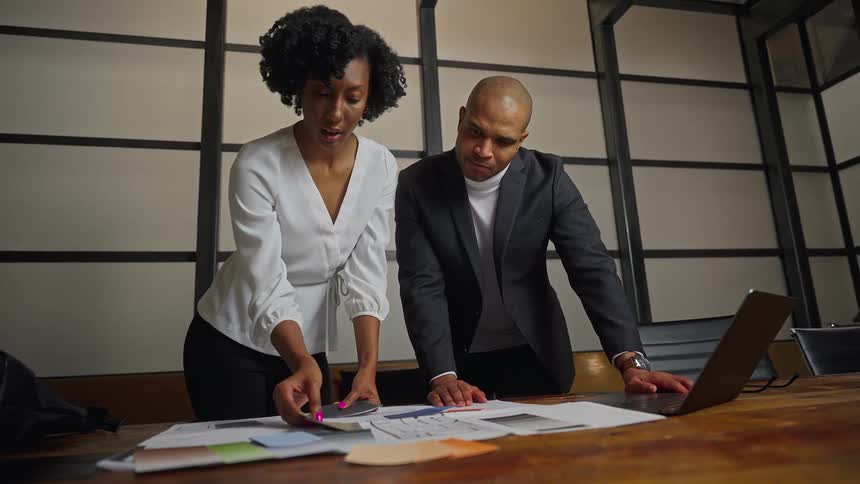 Coworkers stand at table consulting laptop and looking through color strips