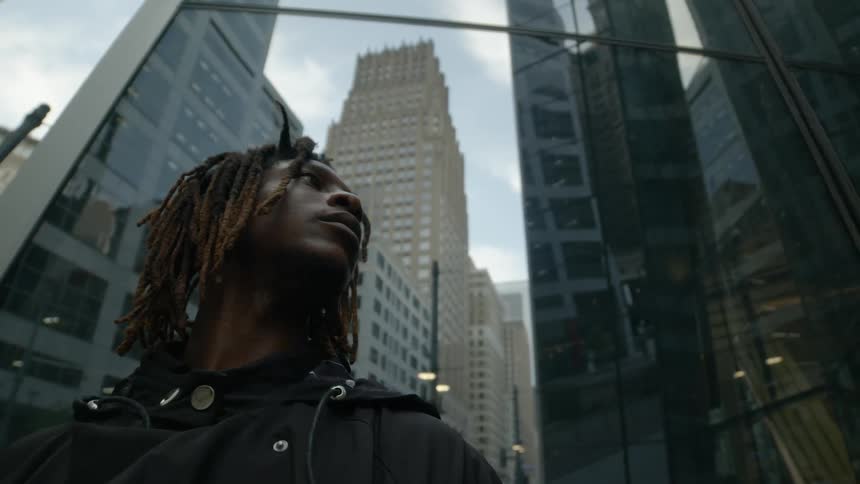 A teenage boy stands at the bottom of a skyscraper and looks around