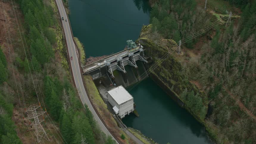 Cars drive on a road in a canyon alongside a river that has a dam
