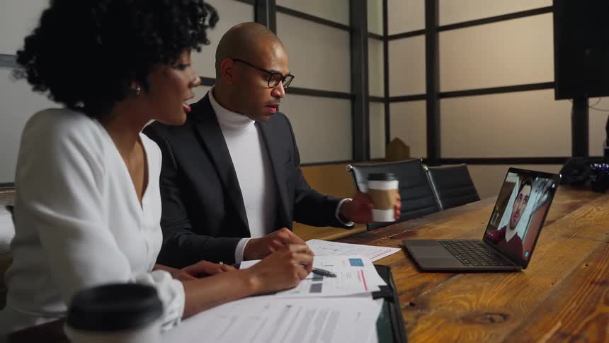 A man and woman chat with a colleague over a video call on a laptop
