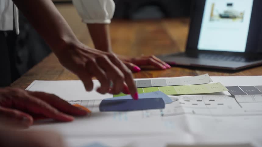 A woman in an office lies some paint samples out on a desk for a man