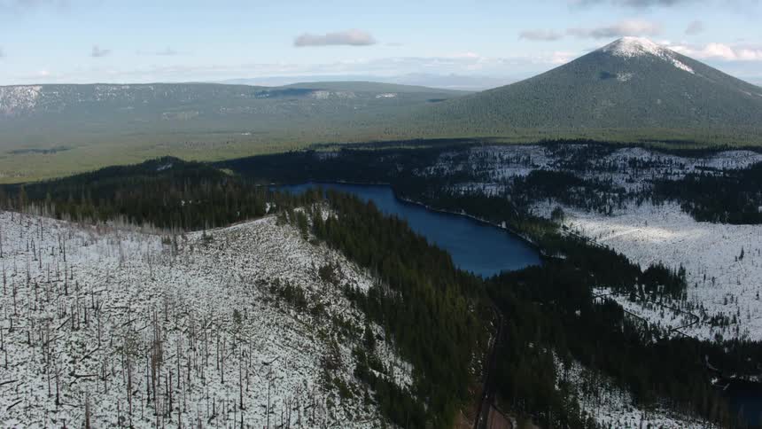 Snow dusted slopes lead down to a bright blue lake with a snow capped mountain behind