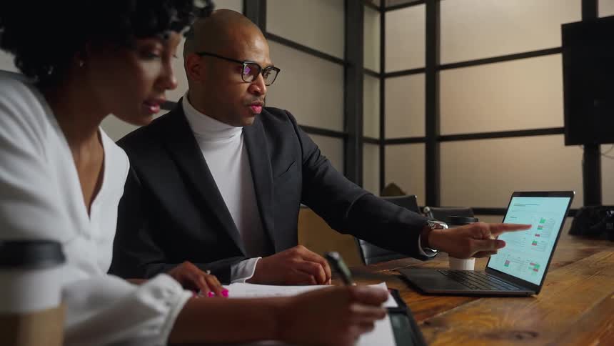 Two people discuss some plans and take notes while looking at a laptop