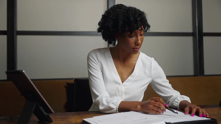 Woman works at desk writing on screen and reviewing documents