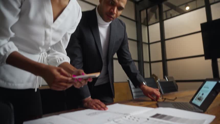 A woman lays down paint chips on a floor plan while meeting with a man in the conference room