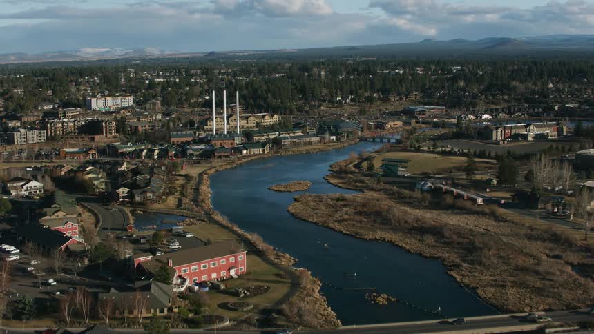 An aerial view of a river running through a city with cars driving across the bridge
