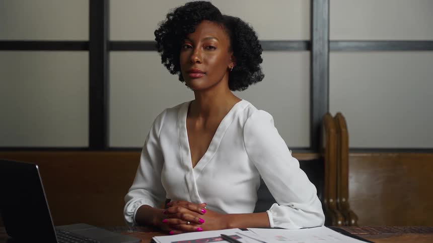A woman sitting at a conference table looks up and poses for a picture