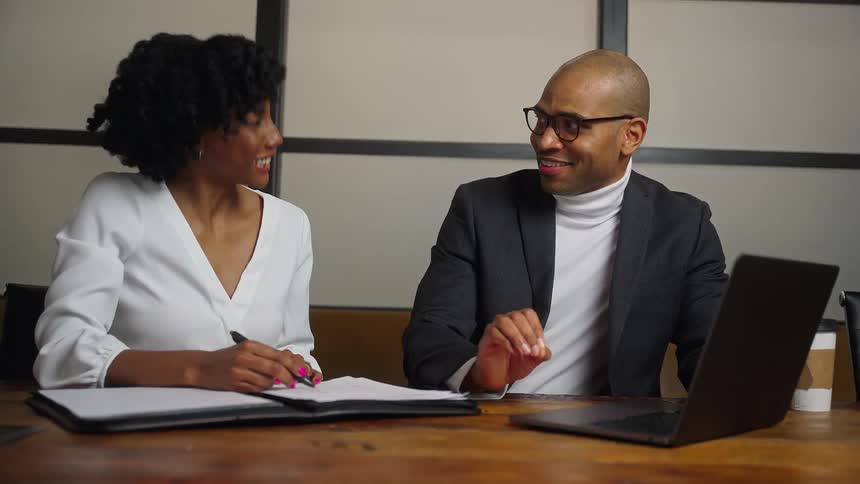 Two colleagues chat over paperwork in a conference room