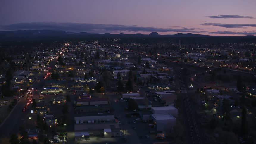 Lights on automobiles shine as traffic moves on the streets around a city as the sun has set and there are mountains on the horizon