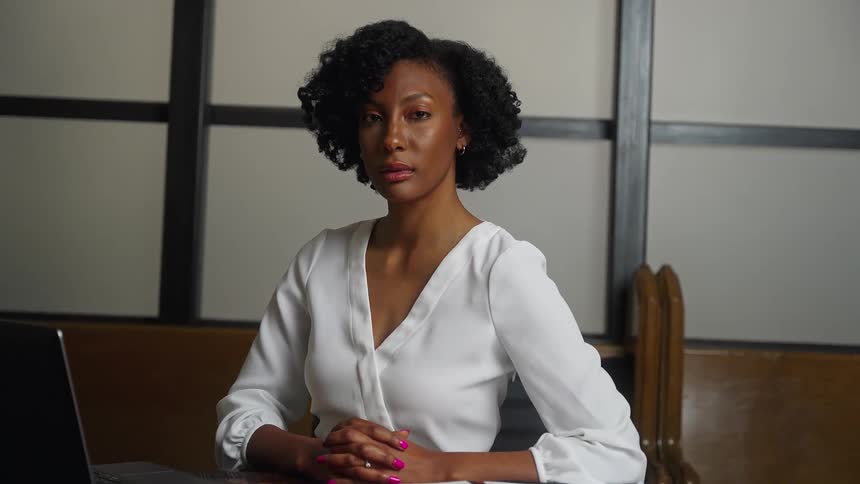 A woman looks into the camera while sitting at a desk indoors during the day