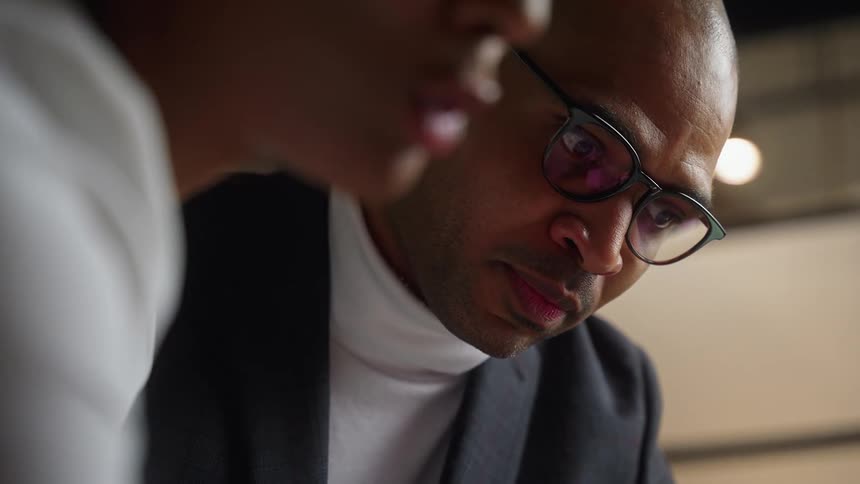 A man and a woman sitting together are looking down at something and talking