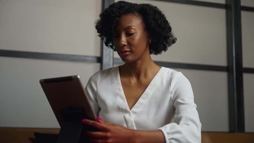 A woman uses a computer tablet while sitting at a table indoors during the day