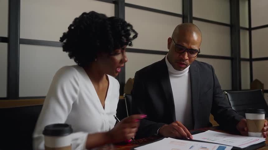A man and woman sit in an office and talk as they look at papers