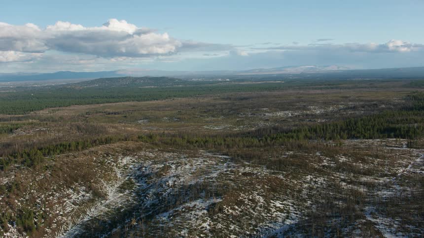 Forested hills and mountains with light snow cover and cumulus clouds in the sky