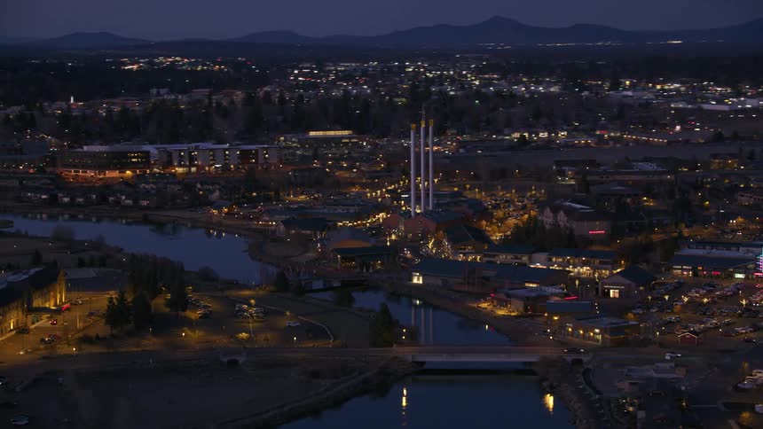 Traffic crosses river over bridges in brightly lit city stretching to misty mountains on the horizon at night