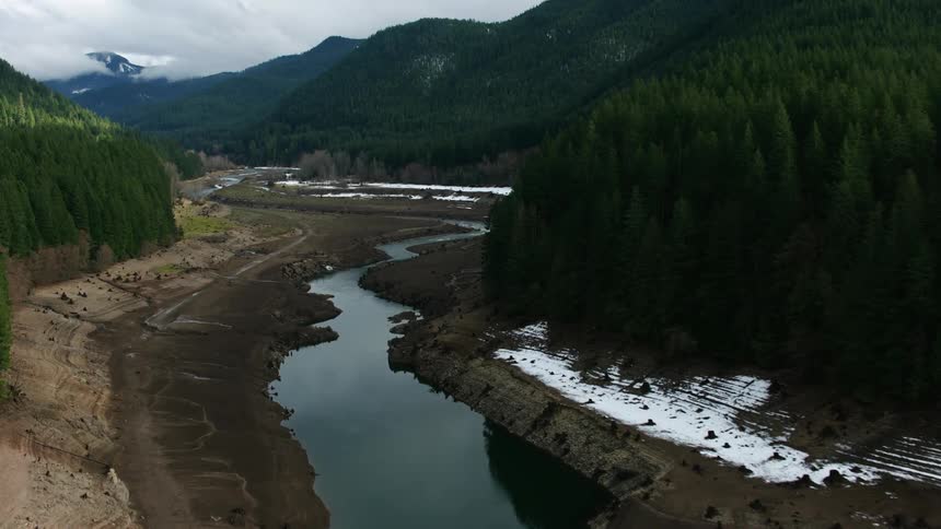 A winding stream with melting snow on the banks and a mountain peak in the clouds