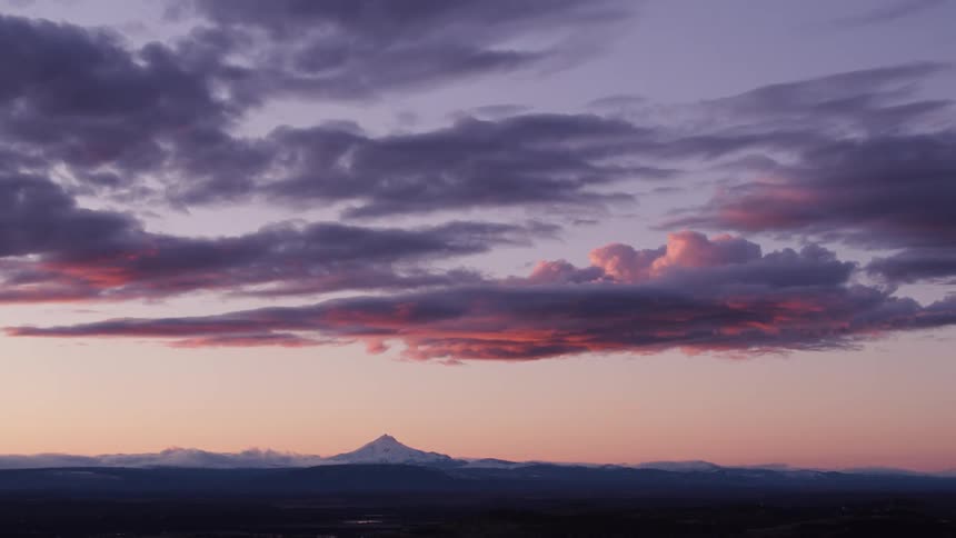 Clouds hanging in the air above flatlands and brush with a mountain on the horizon