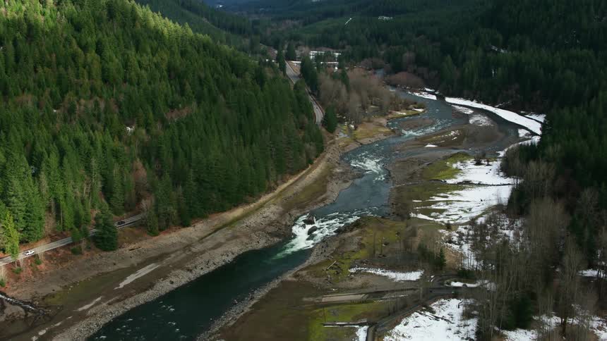 A roadway passes through a stunning river valley within a forested mountain pass
