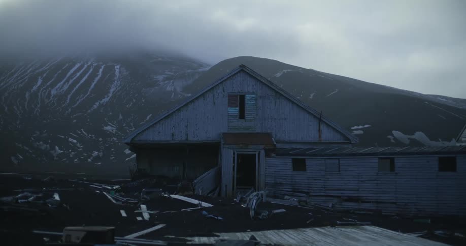 A delapidated old building sits in the snowy mountains