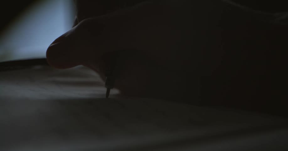 The silhouette of a hand holding a pen writing on fabric