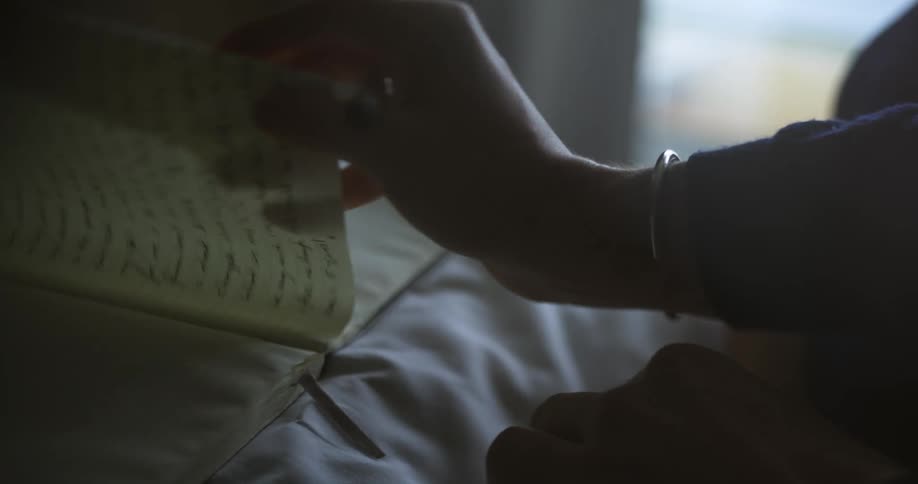 A person turning the page of a notebook resting over a white bed sheet