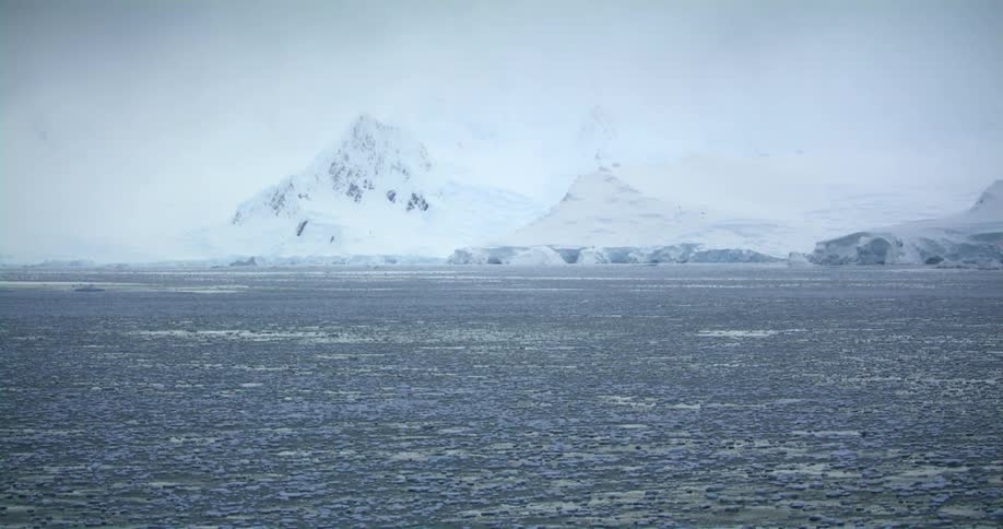 Pieces of ice are in the water as it ripples and waves and there are snow covered mountains in the distance
