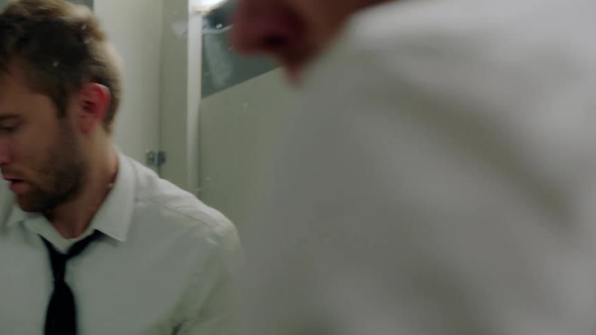 A man looks over his should while distressed as he stands alone in a bathroom