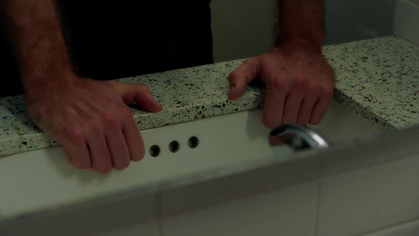 A man is gripping the side of a sink in a bathroom