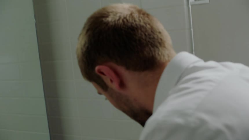 A man looks over his shoulder nervously as he stands alone in a bathroom