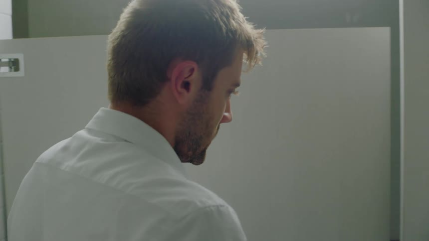 Man looks around restroom including in stall before leaning against sink with his head down