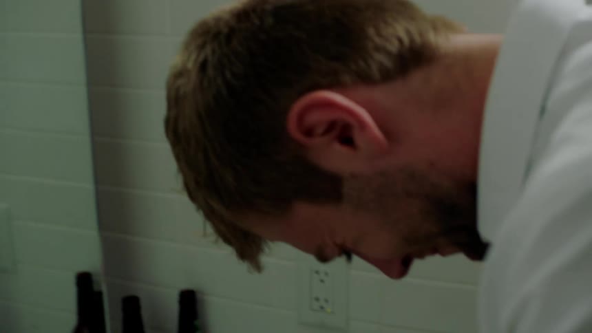 A man is in a small bathroom in front of a mirror and looking down