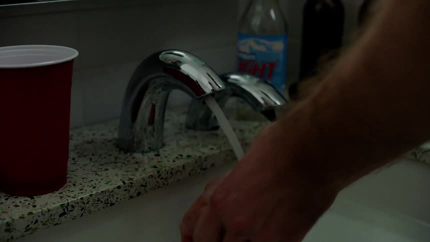 A man holds his hands under a faucet while washing them over a bathroom sink