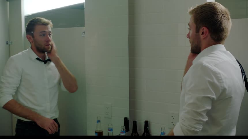 A man with his tie flipped over his shoulder dries his hands and wipes his face in the bathroom looking worried
