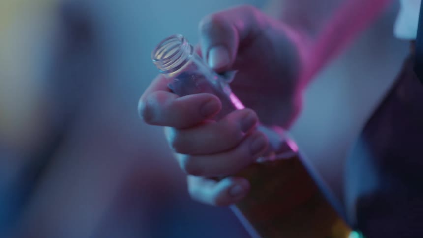 A man is standing and holding a bottle of beer