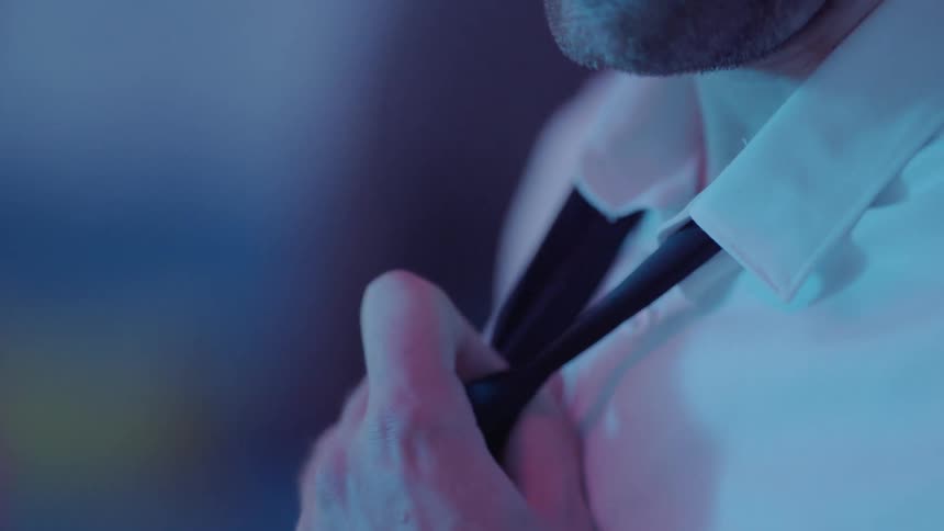 A man wearing a white shirt loosens his tie with his hand as people walk behind him