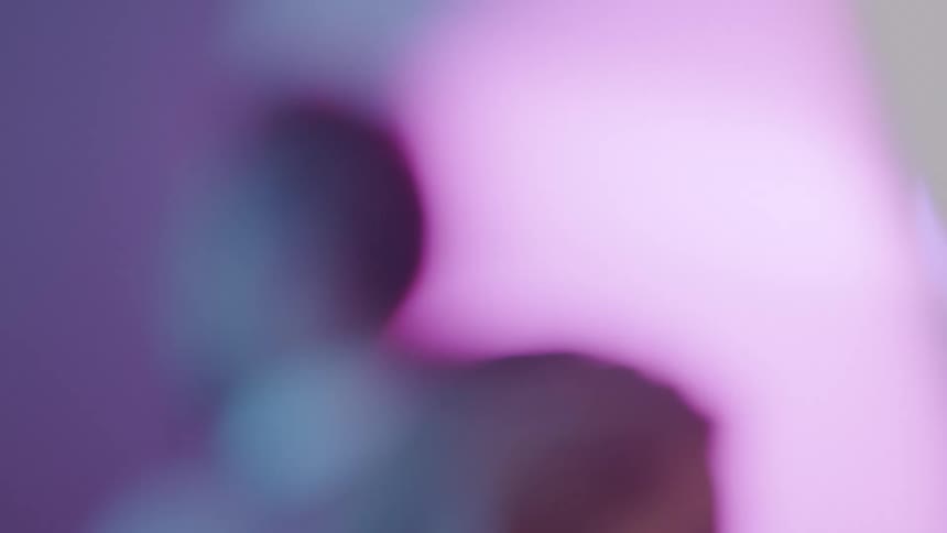 Models walk back and forth in a room with purple walls
